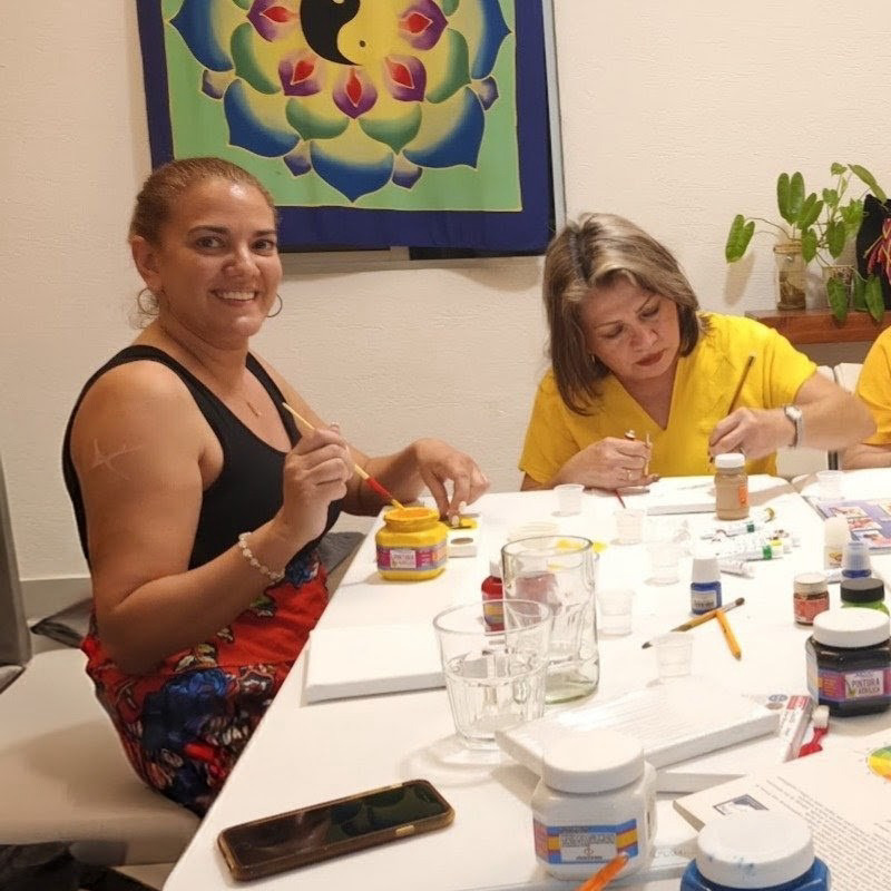 Women creating art together around a table with paints and colorful work